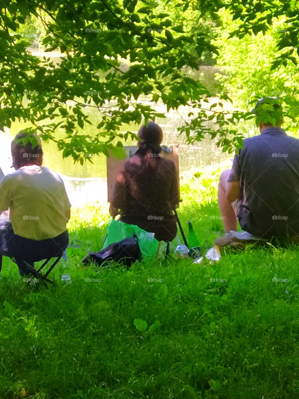 Two girls and a guy are sitting on the banks of the river and painting