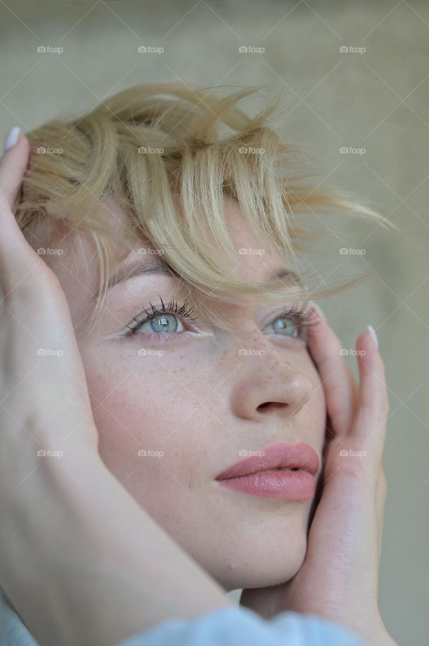 Portrait of a cute girl with blond hair with a beautiful look with her hands near her head