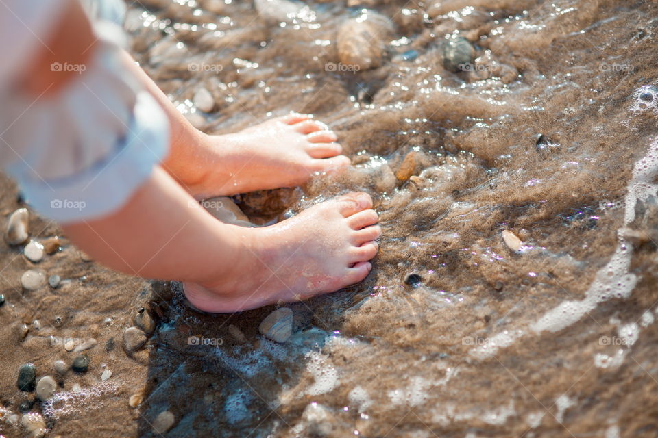 Little girl walking on the sea shore at sunny morning. Legs