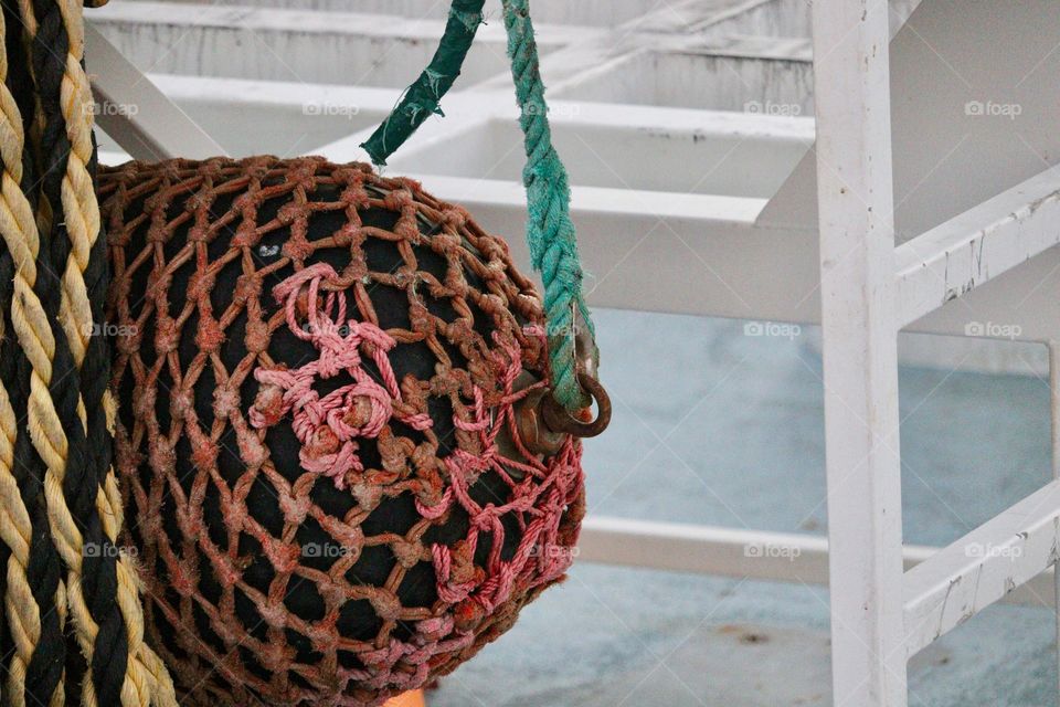 Nautical commercial fishing boat trawler bumper buoy covered in rope netting and tied to boat structure with teal aqua turquoise colour line