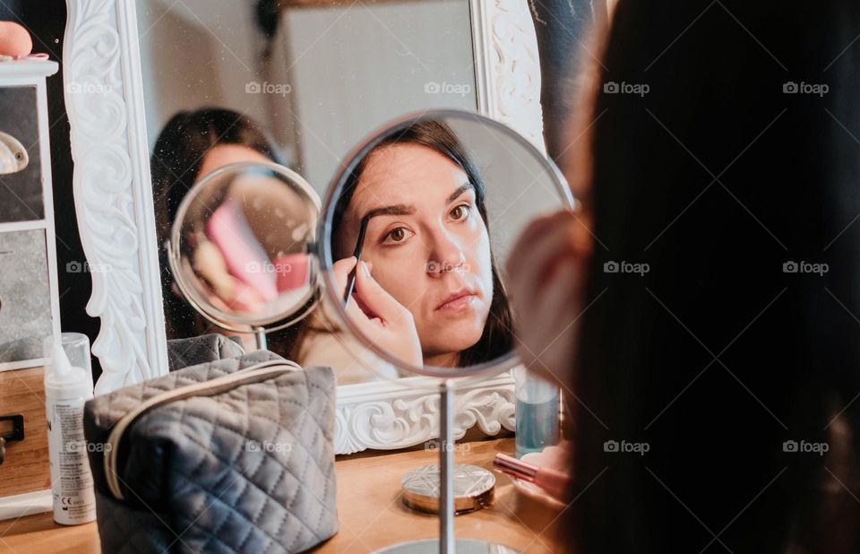 Close-up of a woman doing make-up in front of small mirror