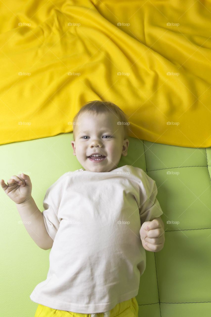 A portrait of a child sitting at home on a green sofa depicts different emotions in yellow shorts.