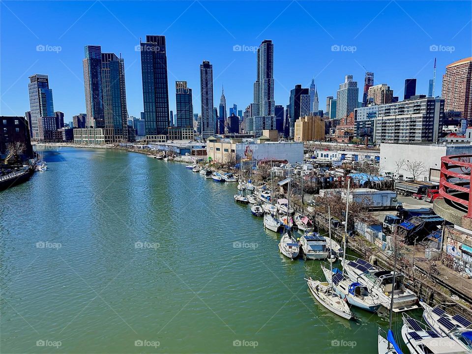 This is beautiful “Newtown Creek” with its many boats seen from the “Pulaski Bridge” that connects LIC, Queens to “Greenpoint”, Brooklyn. In the far distance we can see “Manhattan” incl. the “Empire State Bldg”. 2024. Hypnotic Productions