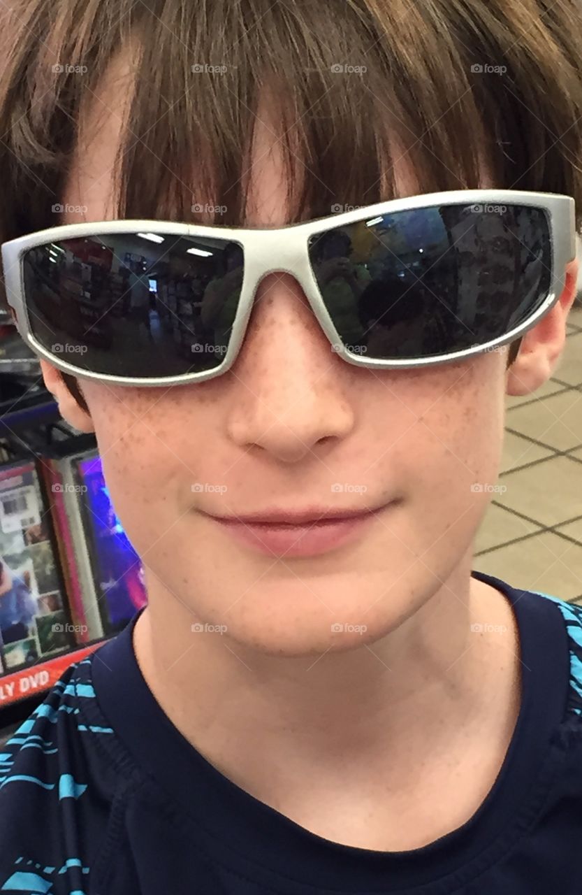 Smiling 10 year old boy with sunglasses he is trying on in the store.
