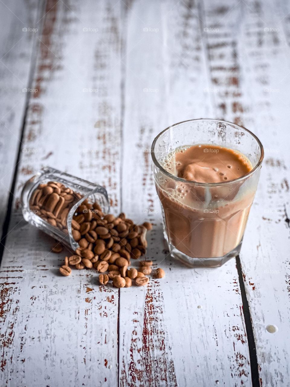 Caffe latte and spilled coffee beans on a white wooden table