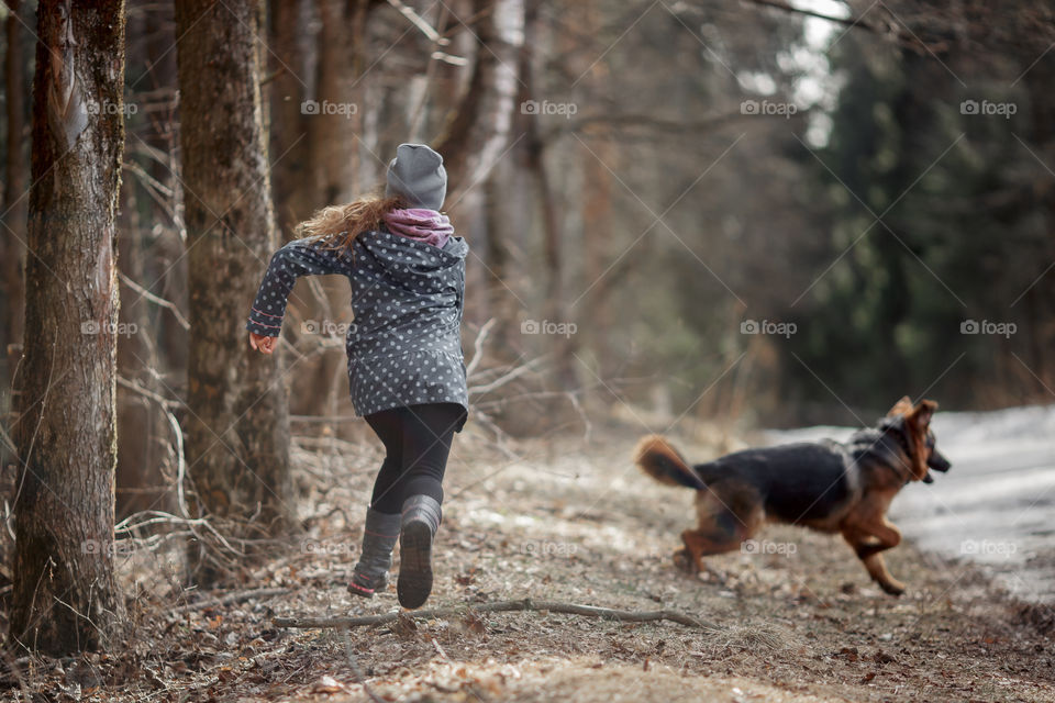 Girl playing with German shepherd puppy in a spring forest at sunny day 