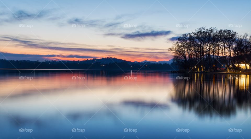 Sunset on a lake with a colorful reflection of the sky, the clouds and the panorama on the water