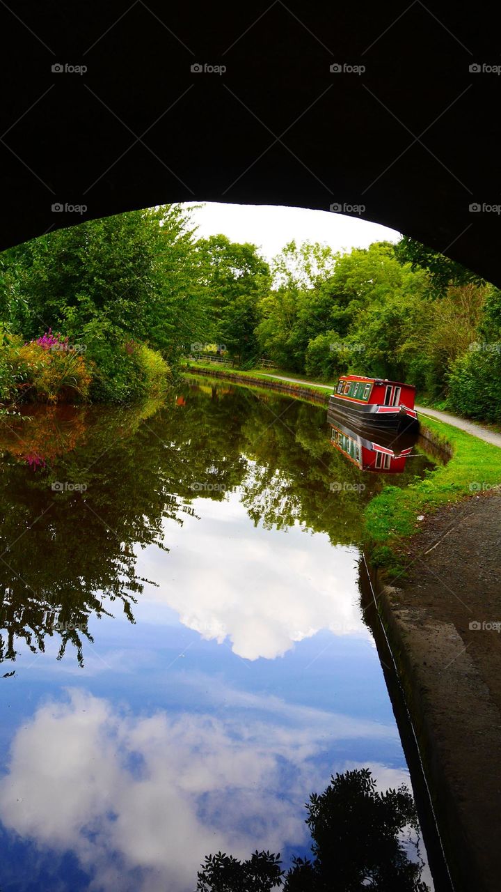 Longboat on canal waterway with reflection of plants and clouds on countryside Wales uk