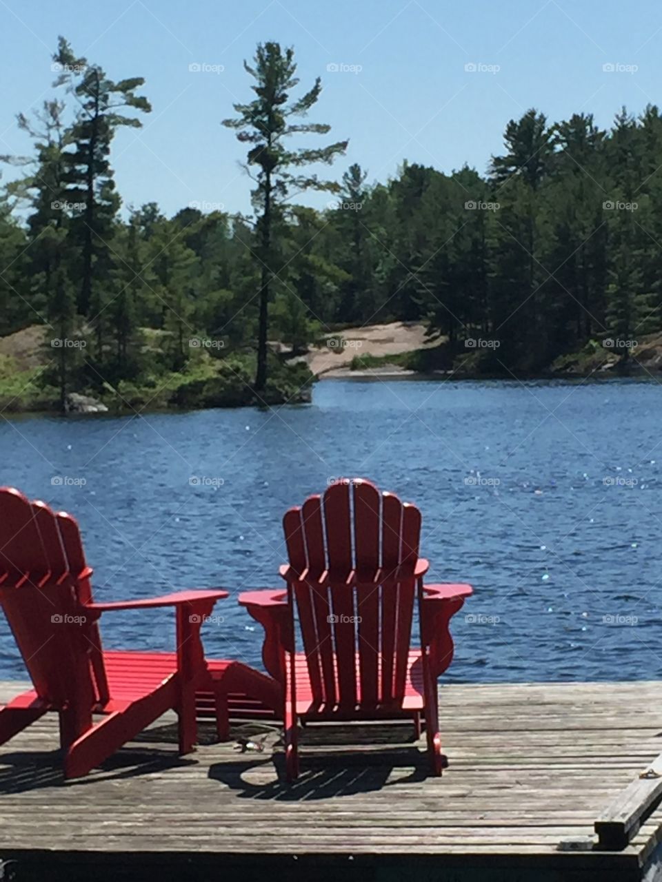 Beautiful tall pine set on the far  shore line the  sun dancing off the water two chairs await you to sit relax and enjoy all that nature has to offer.