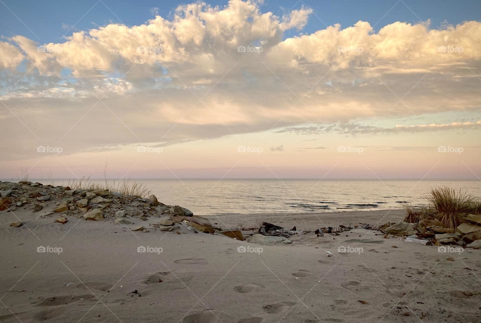 Liquid Fresh water Lake Eerie on Cedar Point shoreline and sandy, rocky beach with purple and blue sunset sky divided by a white puffy cloud 