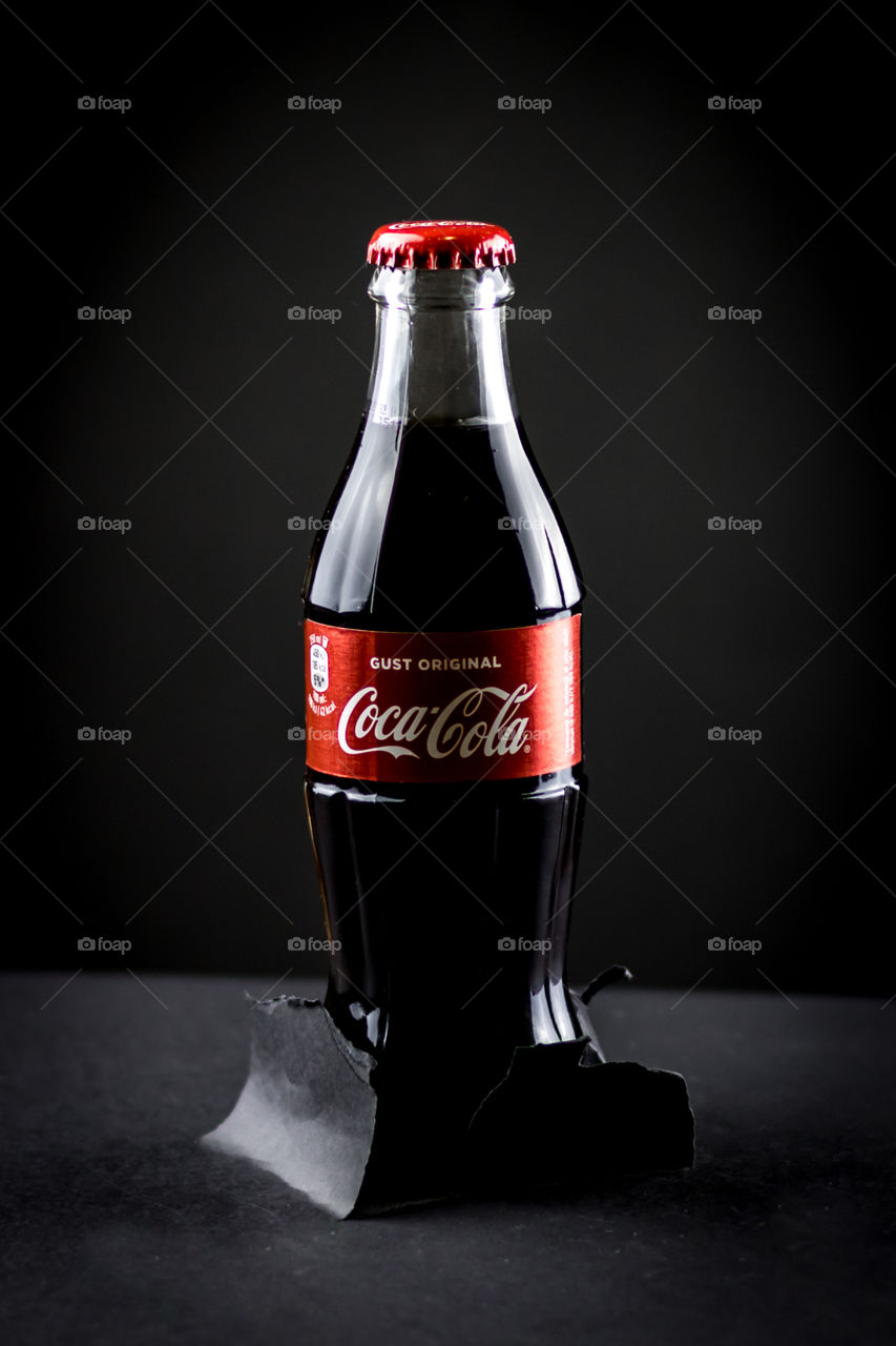 Glass bottle with Coca-Cola on the dark background.
