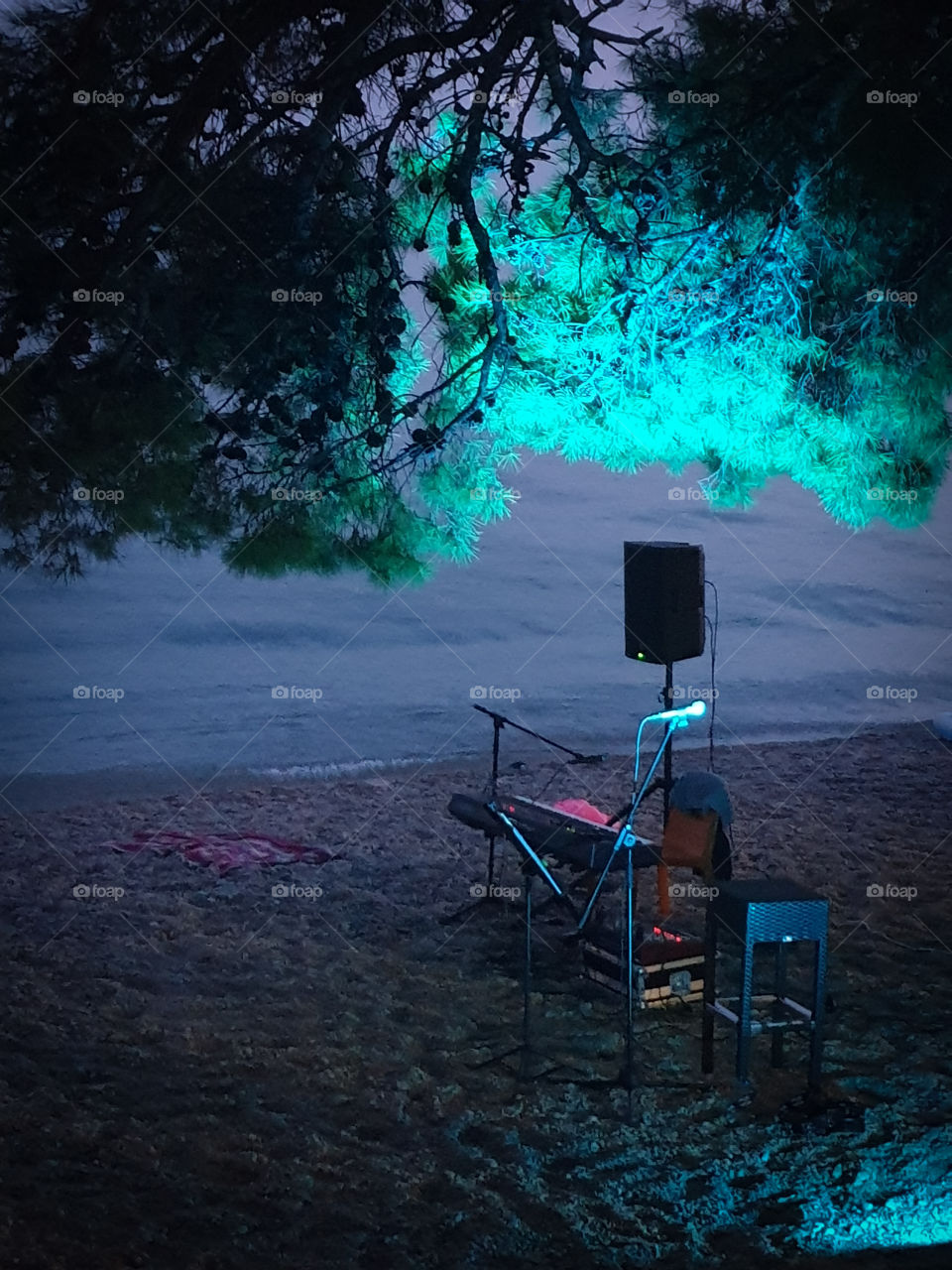 Summer evening on the warm south sea.  Preparing for the performance.  A microphone with a synthesizer and speakers standing on a pebble beach under pine trees with backlight