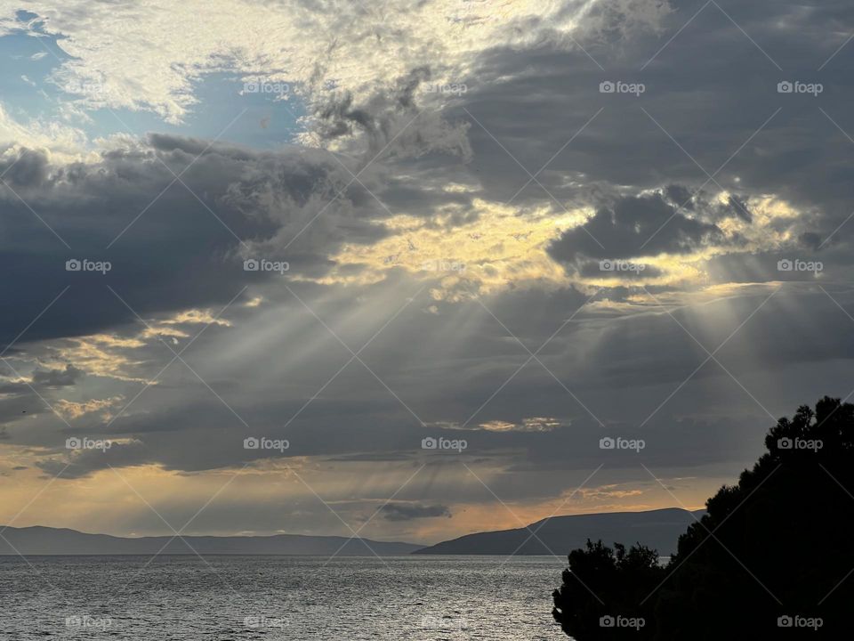 Stunning landscape view to the horizon over the Mediterranean sea with sun rays breaking through the dark thunderstorm clouds