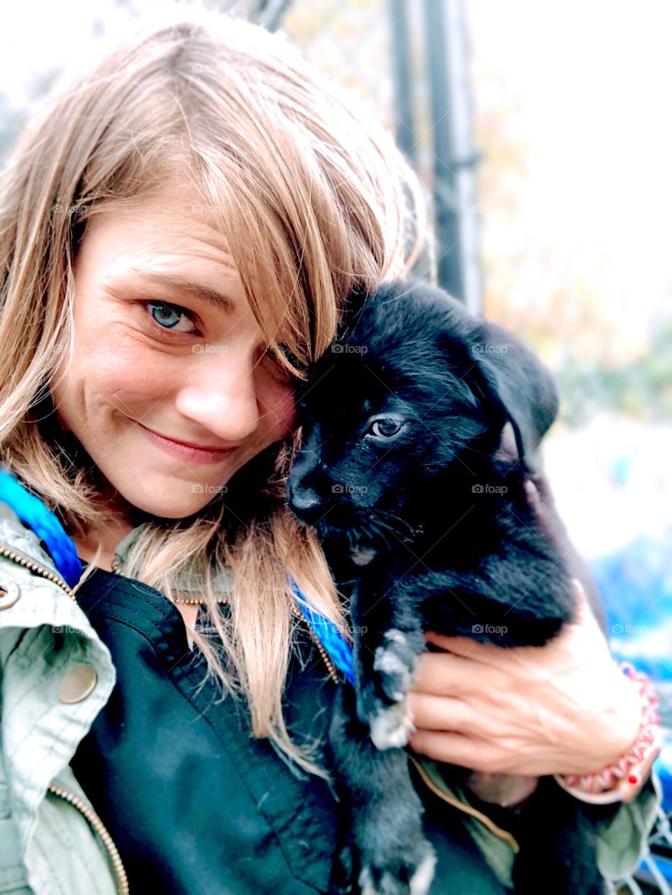 Close up portrait of young blonde girl holding small,  black puppy
