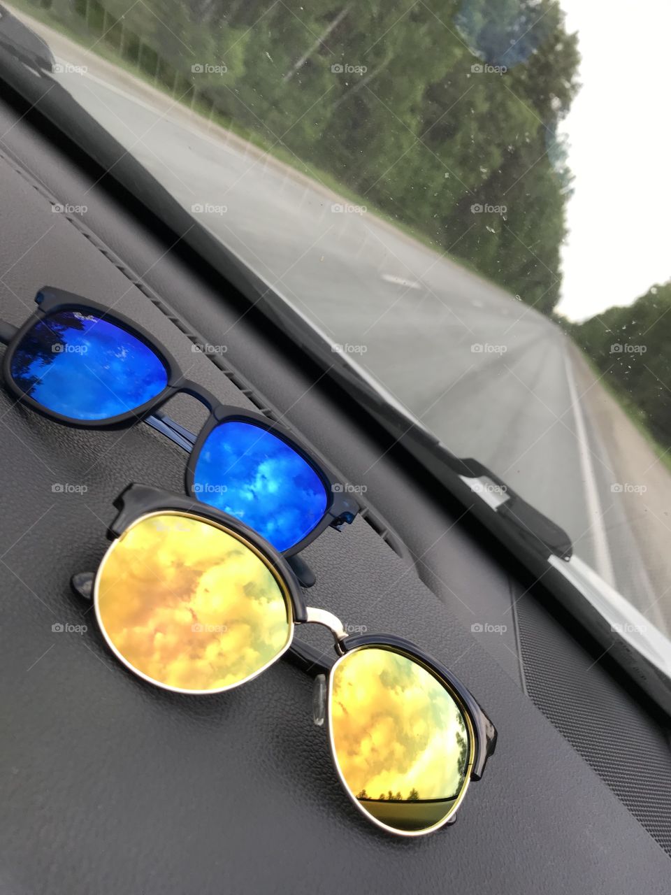 Multicolored sunglasses on the panel in the car. The sky is reflected in the sunglasses.
