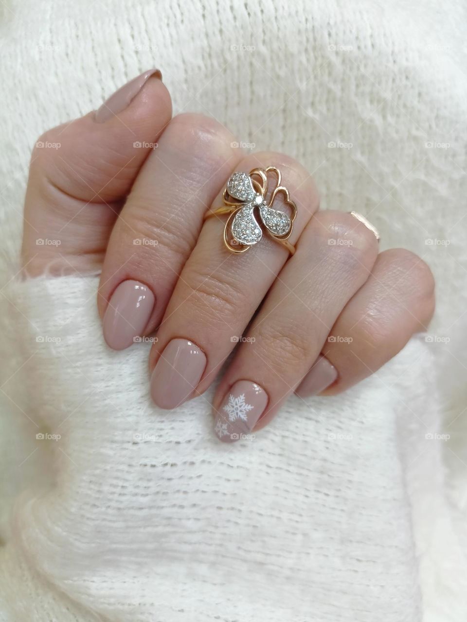 manicure on a female hand, the color of nails is coffee with milk, a white snowflake, female hands on a white background, a warm fluffy scarf, nail polish, a gold ring on a finger, a female hand with a ring