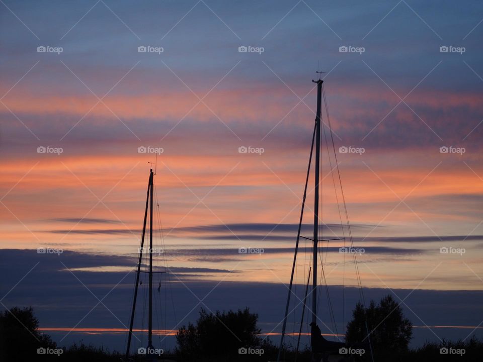 Such a beautiful summer evening, orange, blue purple colors in the sky. Peaceful and quiet. Two masts of sailingboats. Great summerfeel