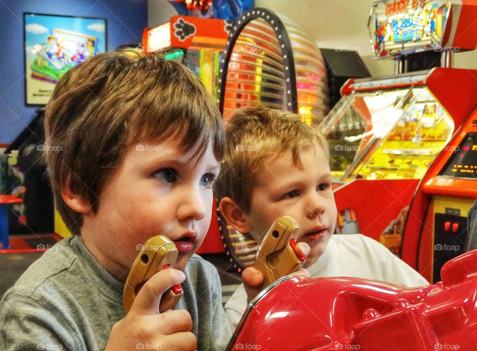 Little Boys Playing Shooter Games At A Video Arcade. Young Boys Playing Videogames