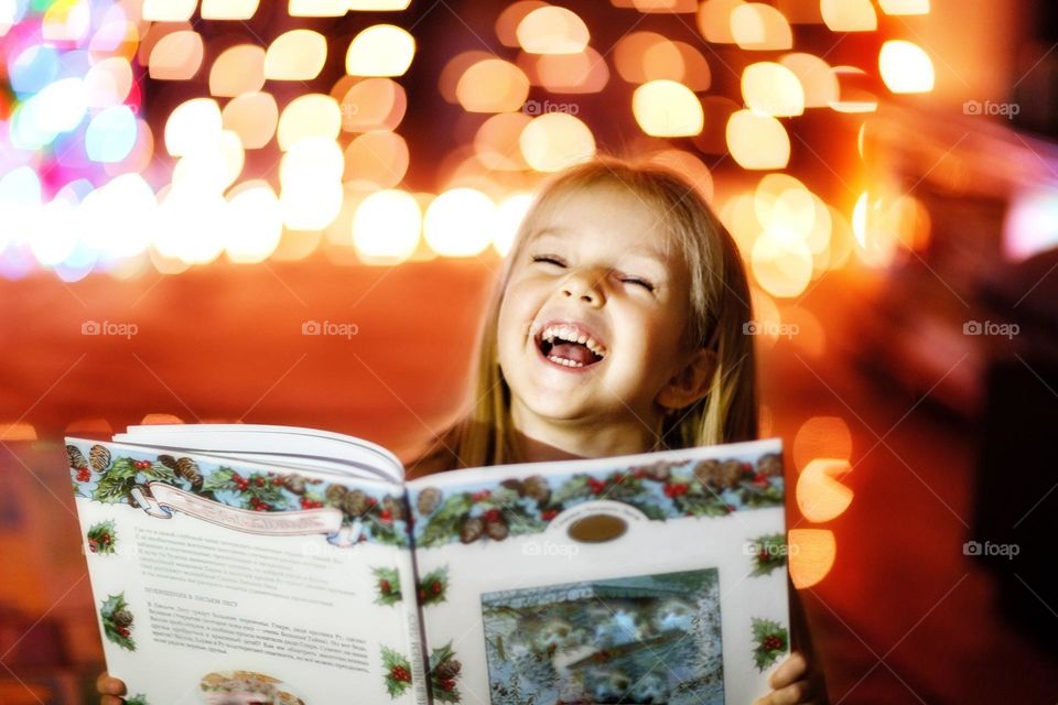 Happy Caucasian little girl laughing at home when reading fairytale book 