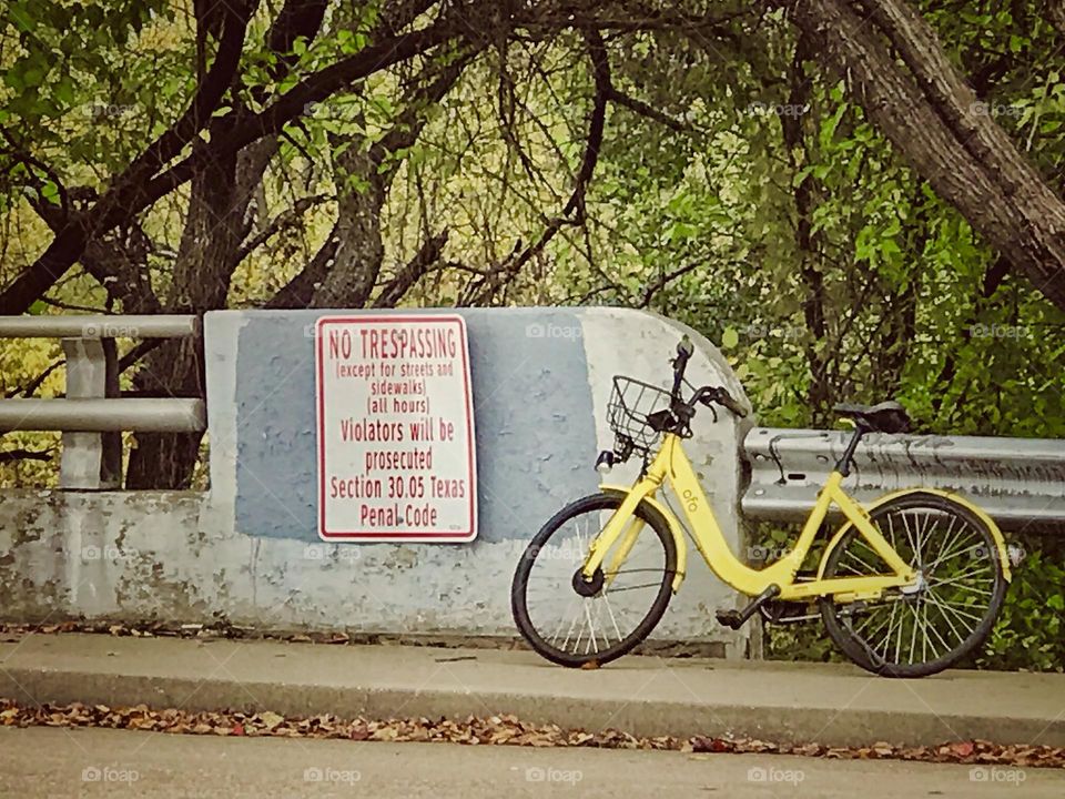 Lone yellow bike unaccompanied on a bridge by a no trespassing sign.