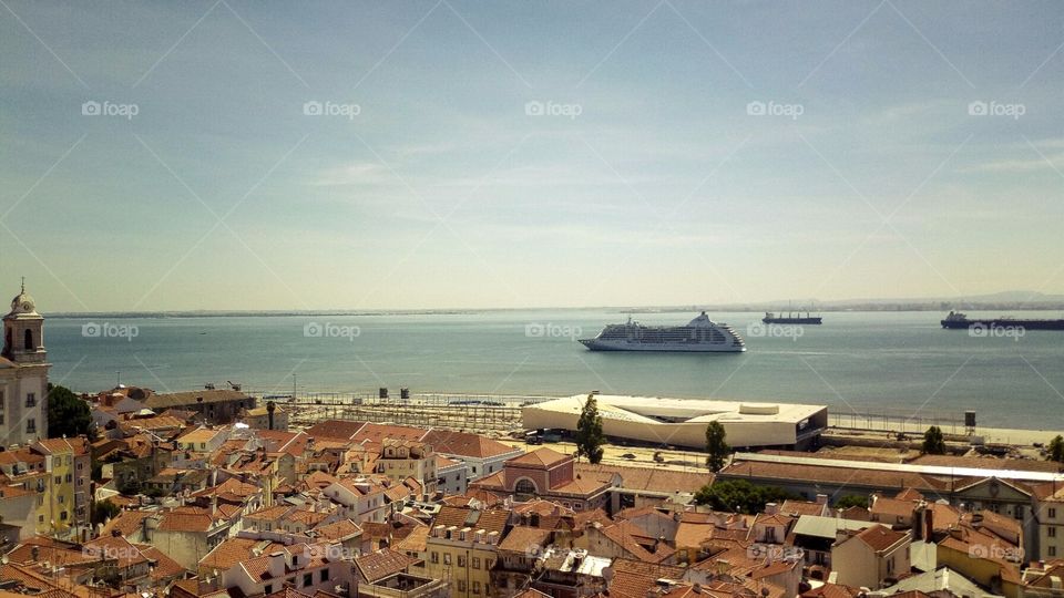 Clear blu sky Panoramic view of some rooftops in Lisbon and the Tago River with a cruise ship on it.