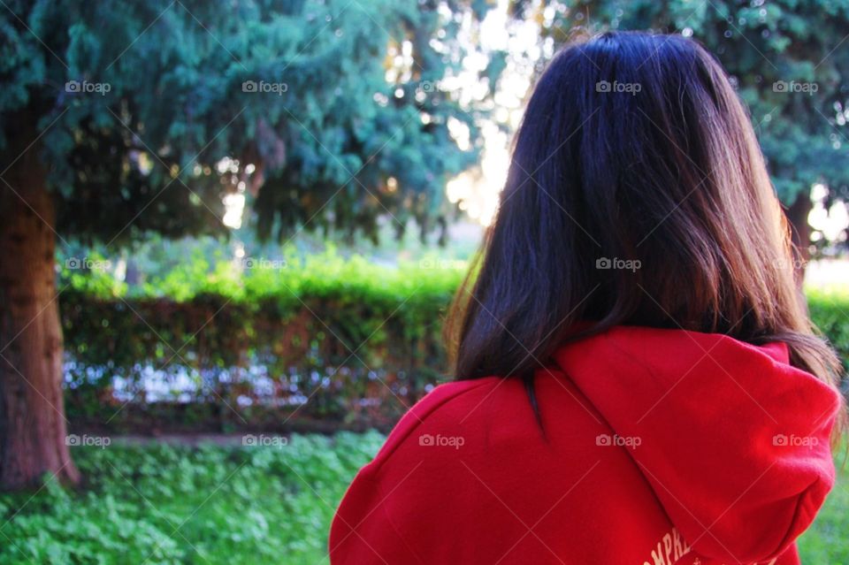 Girl thinking, back, in a garden, green, wearing red hoodie.