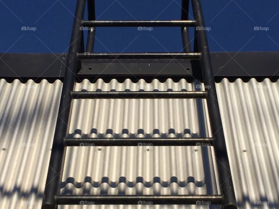 Black ladder on side of building leading up to big blue sky