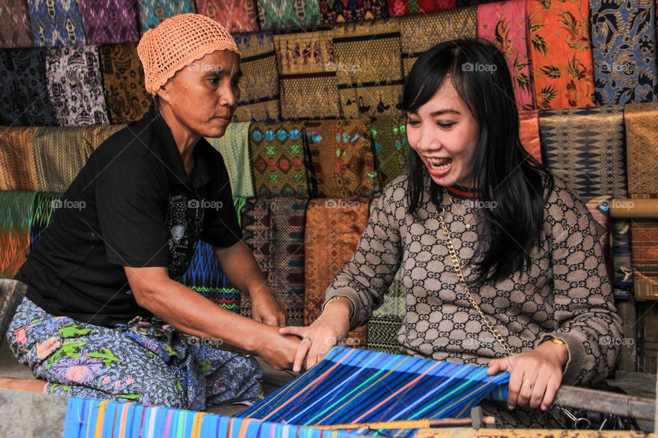 Portrait of a young woman sitting learning to weave cloth with traditional tools at a traditional cloth craft workshop in Sade village, with a happy expression, Lombok, Indonesia.