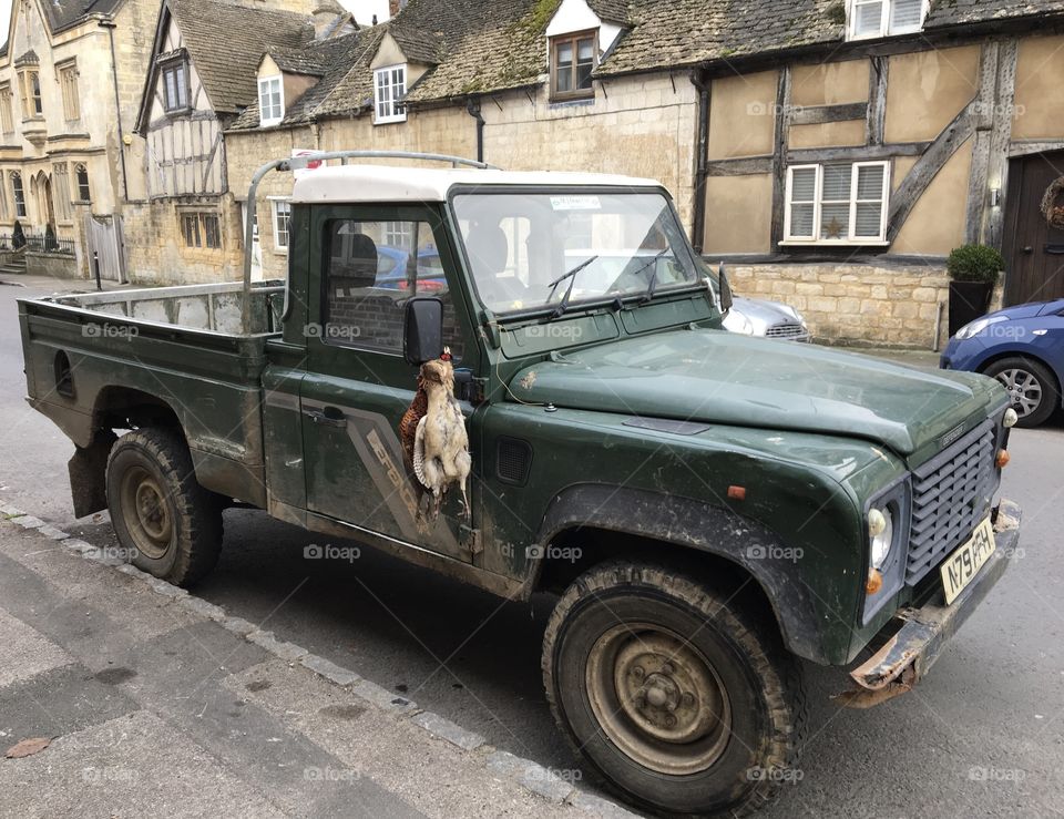 A brace of pheasants hanging outside a jeep tied onto the wing mirror 