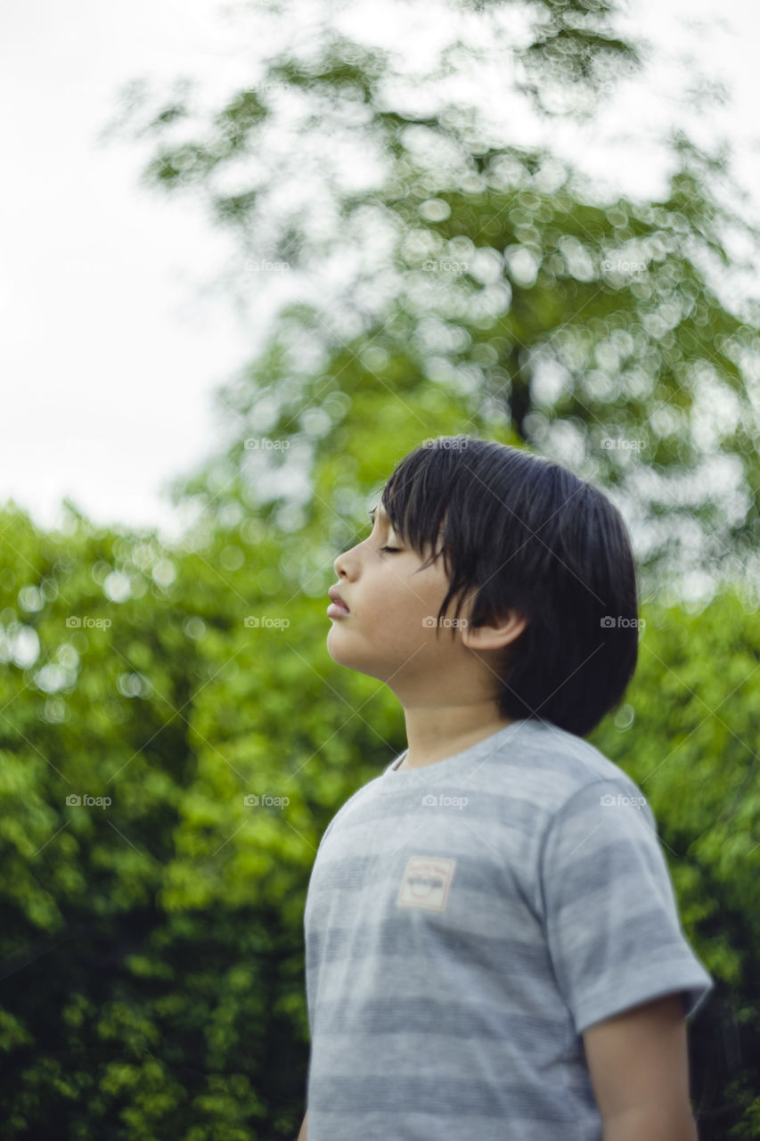 outdoor portrait of relaxing young eurasian boy on a blurry out of focus bokeh foliage background