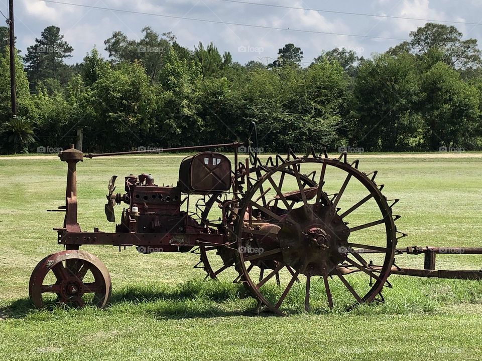 An antique iron tractor sitting on a field Keith trees as backdrop against shy. 