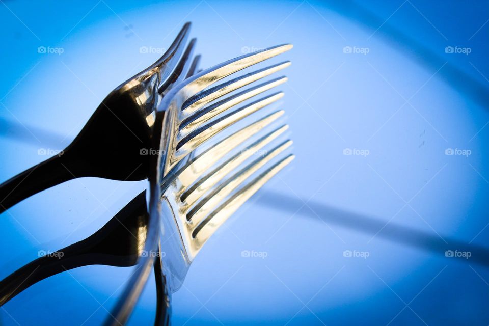 Metal fork is reflected in a mirror.  A fork is a cutlery or necessary kitchen tool