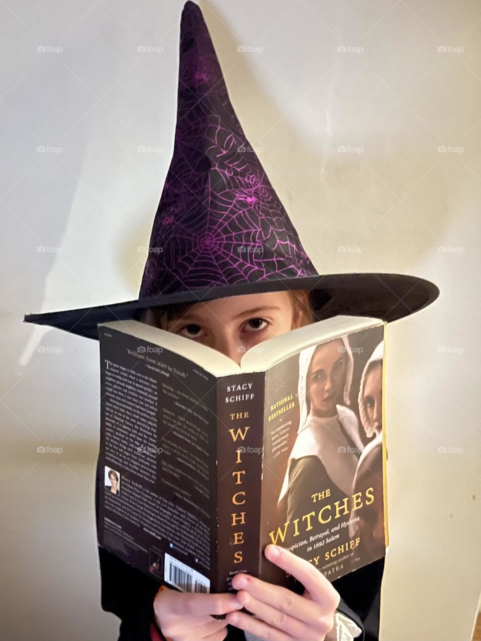 A little girl in a witch hat reading a book about witches.