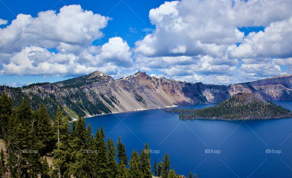 Day picture of Crater Lake National Park, Oregon USA; bright, beautiful landscape photo with Wizard island on the right and fluffy clouds