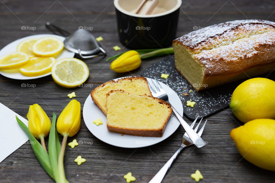 two pieces of lemon cake on a plate, lemons, yellow tulips and decoration