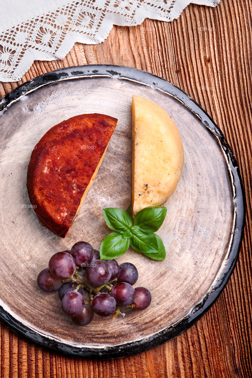 Cheese and black grapes decorated with mint on handmade pottery plate on old wooden table from above