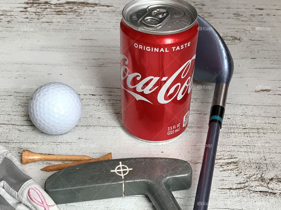 A can of Coca Cola and golf equipment on a rustic white background 