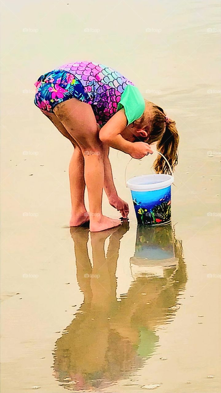 young girl searching and collecting seashells by the seashore. on the sandy beach enjoying the summer vacation
