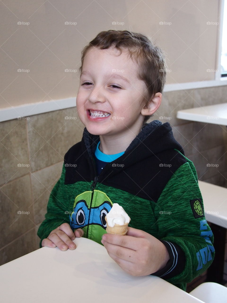 A little boy really enjoys his small vanilla cone that really hits the spot. 