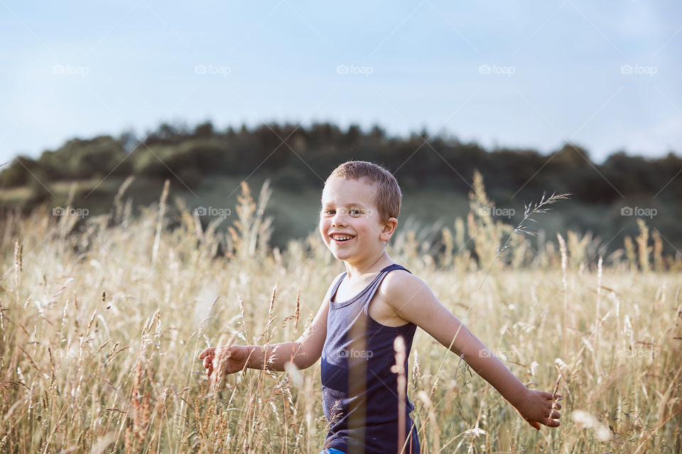 Little happy boy walking through a tall grass in the countryside. Candid people, real moments, authentic situations