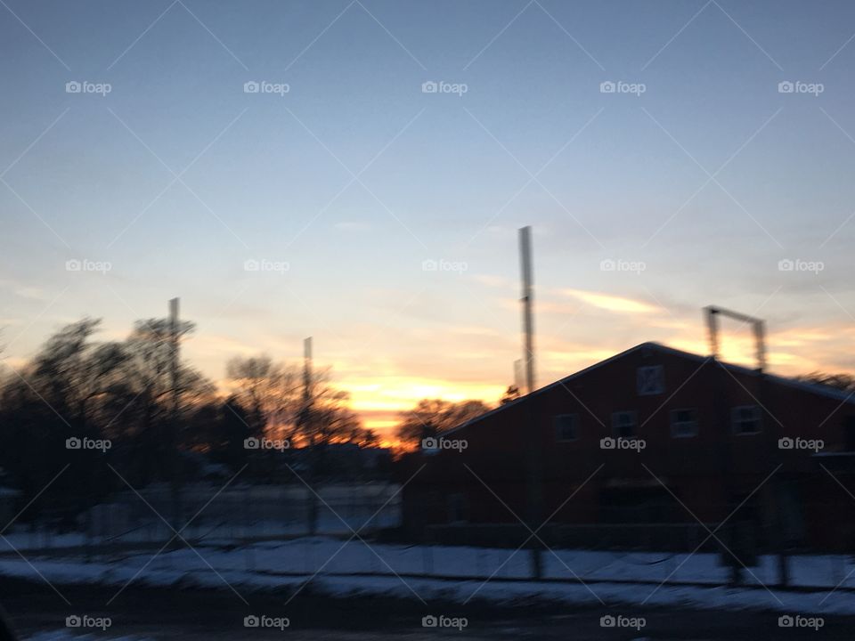 A beautiful sunset behind a snowy abandoned barn taken from inside a moving car.