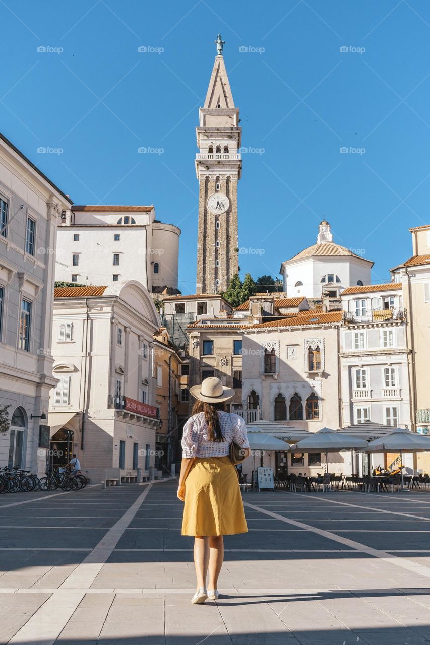 Rear view of woman wearing summer clothes and sunhat exploring the beautiful town of Piran in Slovenia during summer