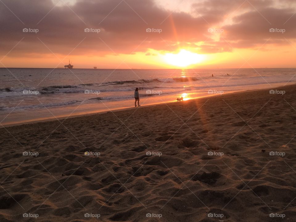 A girl and her dog enjoying an evening stroll on the beach as the sun is setting down on the East