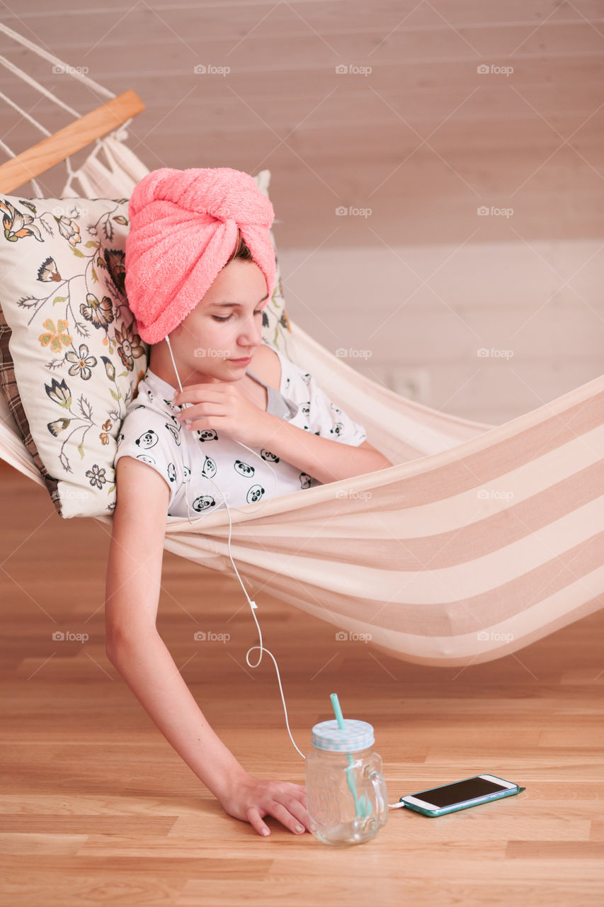 Teenage girl with towel on head using mobile phone sitting in hammock at home