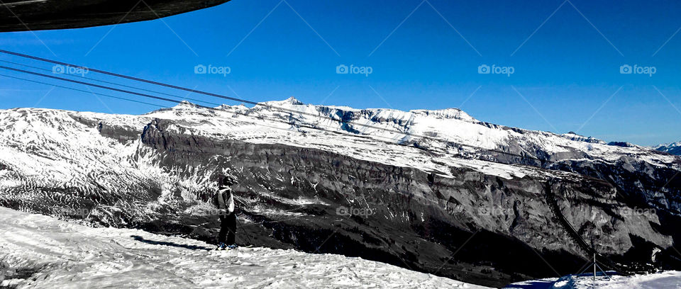 Skier stands on a bright day in the Swiss Alps looking over the mountains