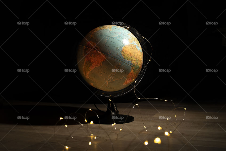 A portrait of a globe surrounded by fairy lights on a wooden floor surrounded by darkness. it is like the lights resemble the stars surrounding our earth.