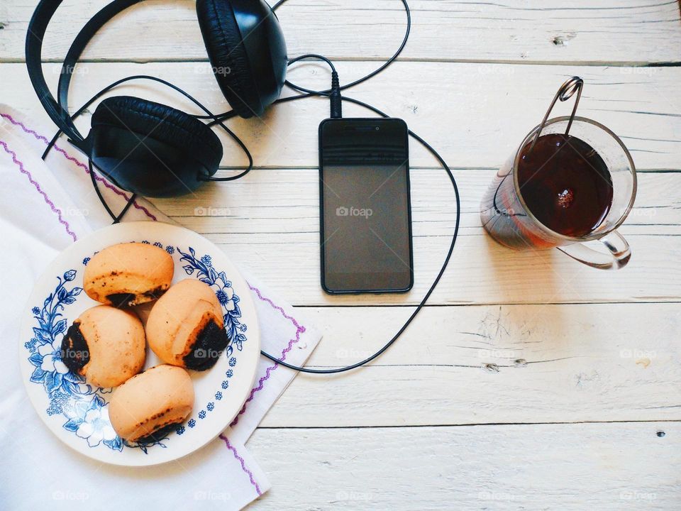 cup of tea, cakes, smart phone and headphones