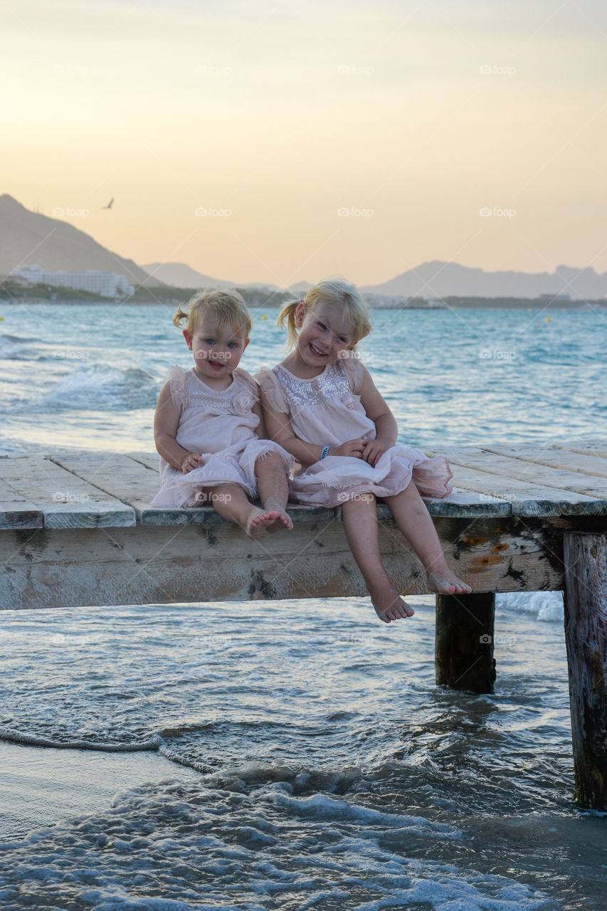 Two little sister sitting on a bridge smiling and looking cute in Alcudia, majorca.
