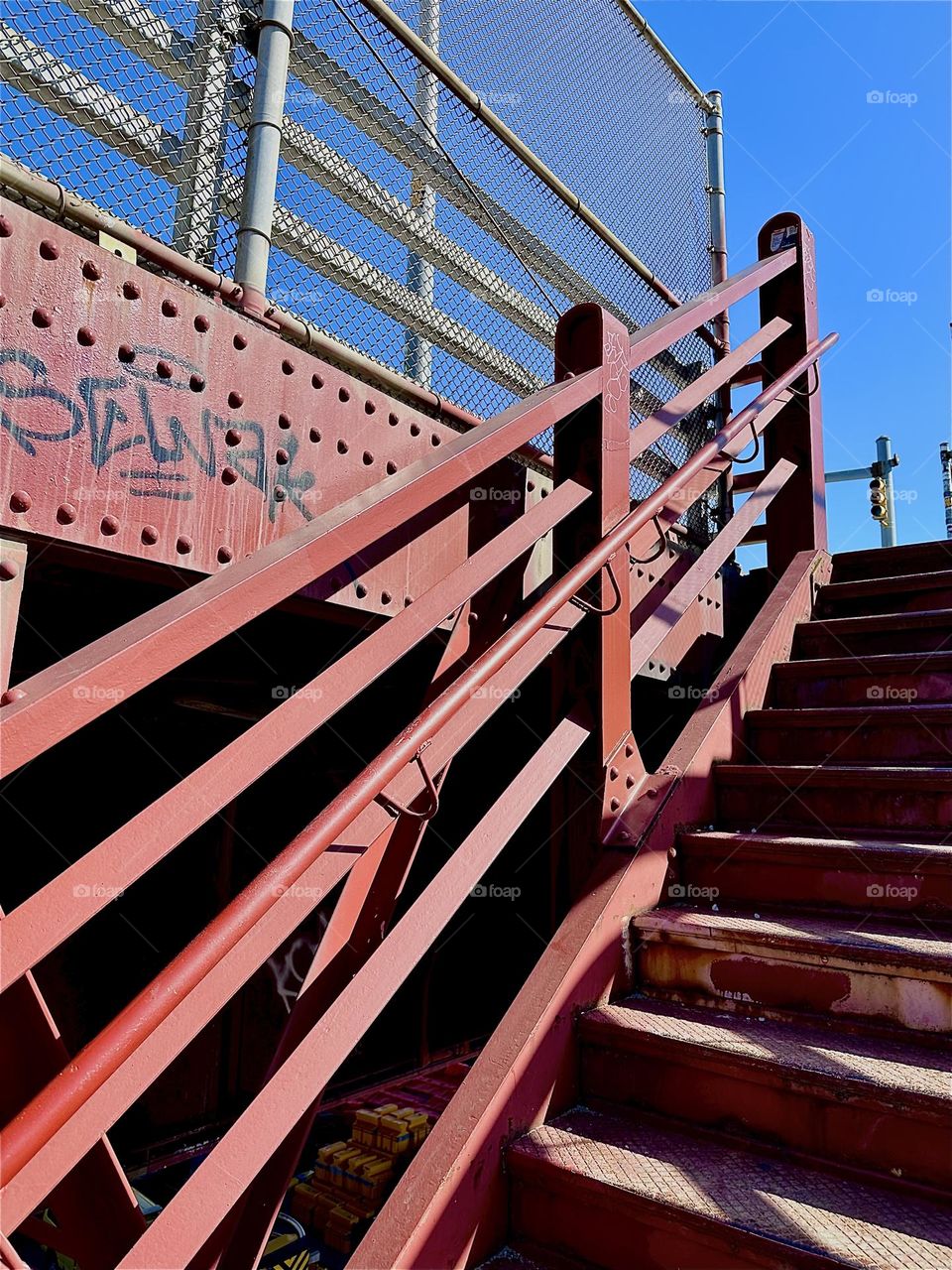 This is the red metal staircase of the “Pulaski Bridge” at “Newtown Creek” ascending on the LIC side of the bridge that leads to “Greenpoint”, Bklyn. The spectacular structures remind of the “Bauhaus” school of the 1930s. 2024. Hypnotic Productions