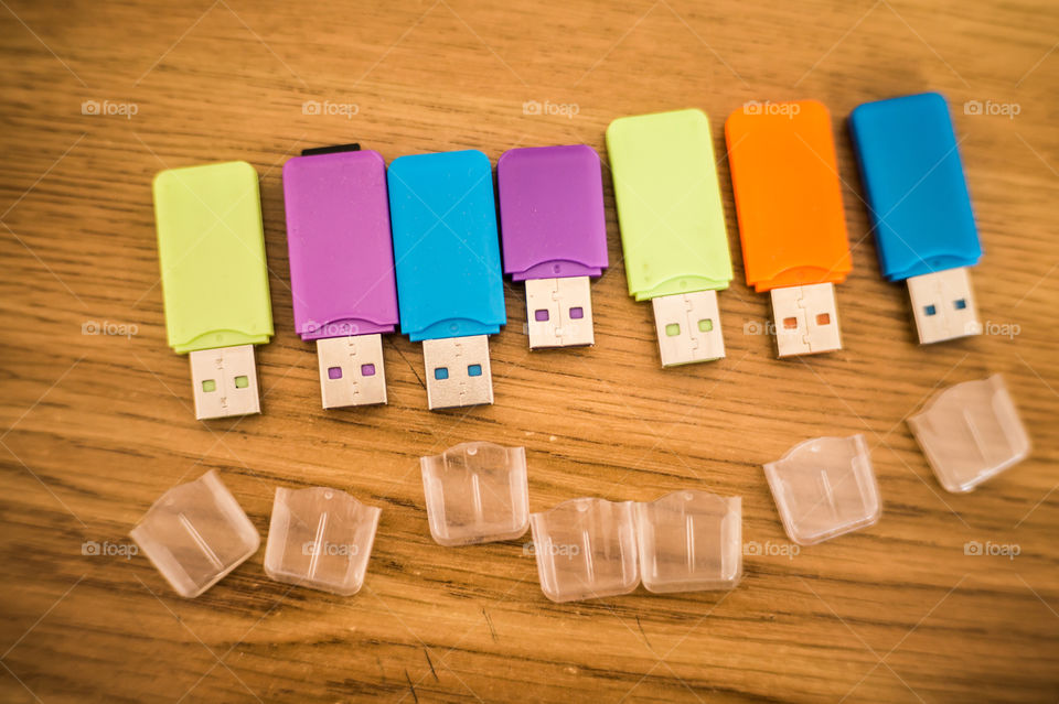 Multi-colored flash drives for working with documents, saving and transmitting, sharing files on a wooden texture table close-up.